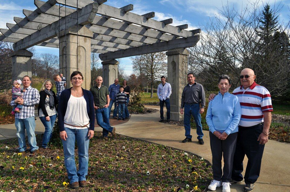 People gather under a pergola structure in a garden setting during an outdoor event.