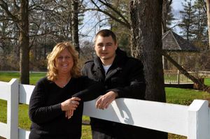 Two people leaning against white fence in backyard setting.