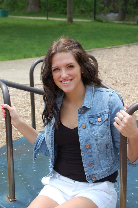 Woman in denim jacket sits on playground equipment on sunny day.