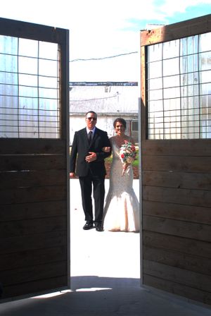 A wedding couple stands in the doorway of a rustic barn entrance with wooden doors and windowpanes.