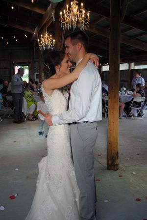 A couple shares their first dance under elegant chandeliers in a rustic barn venue.