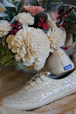 A bridal bouquet with white and burgundy flowers sits next to sparkly white Keds sneakers.