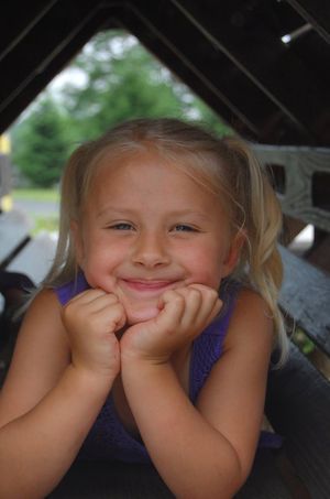 Child with pigtails rests head on hands while lying down and smiling at camera.
