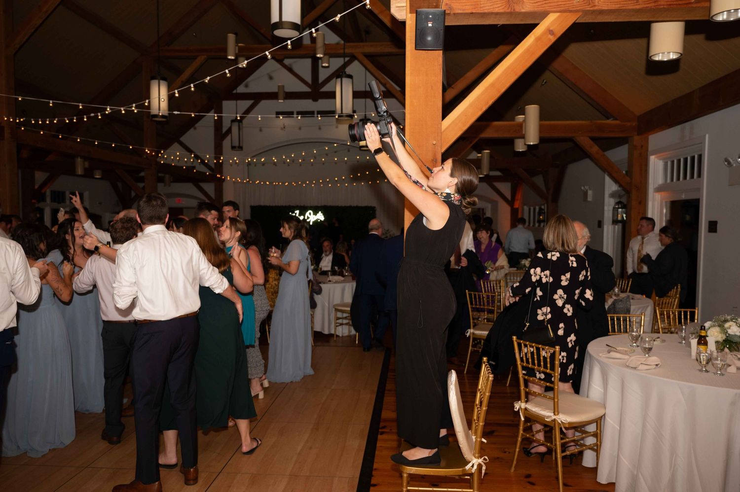 Wedding guests dancing and celebrating in a rustic venue with string lights overhead.