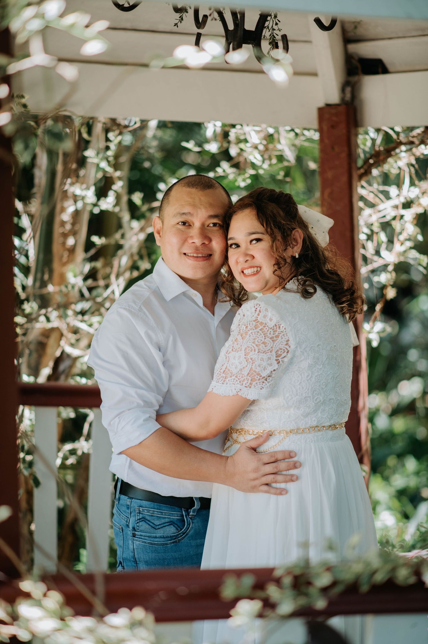 A couple embraces in a wooden gazebo during their wedding photoshoot.