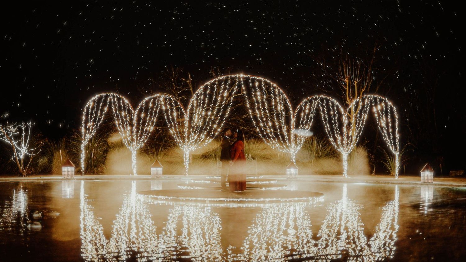 Glowing arch-shaped light installations creating reflections on water at night.