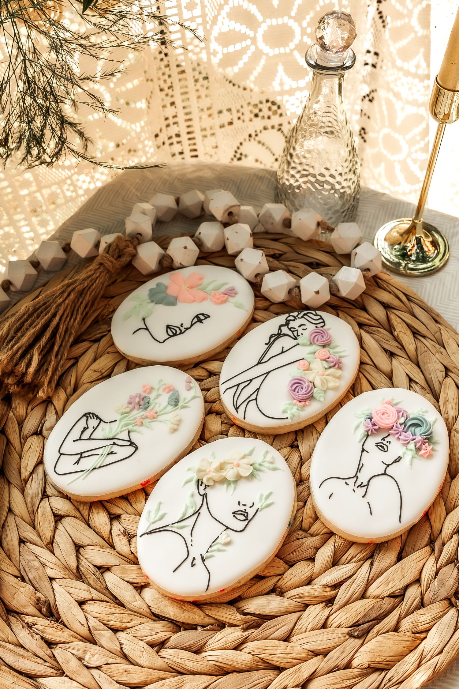 Artistic cookies with delicate line drawings and floral designs displayed on woven rattan charger.