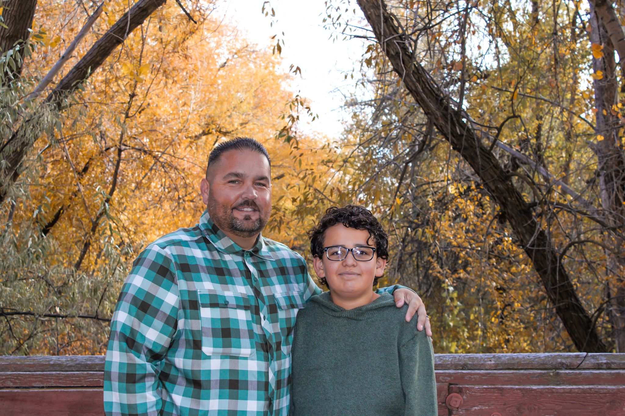 A father and child pose together against a backdrop of golden fall foliage.
