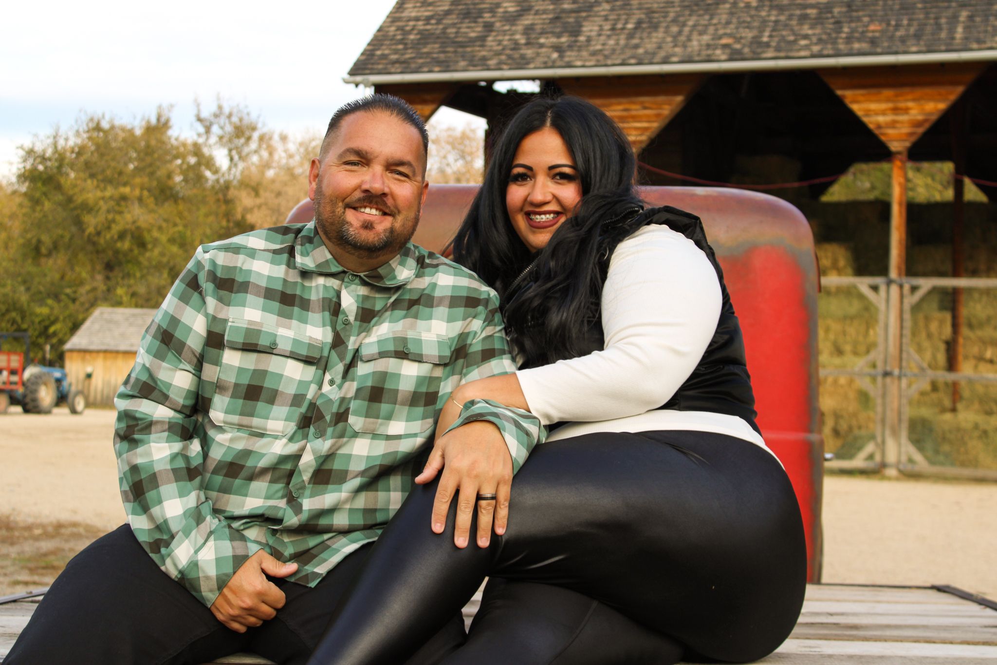 A couple sits together on a rustic wooden bench during autumn.