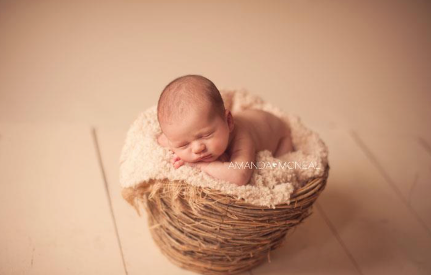 Newborn baby sleeping peacefully in rustic basket with soft cream colored blanket.