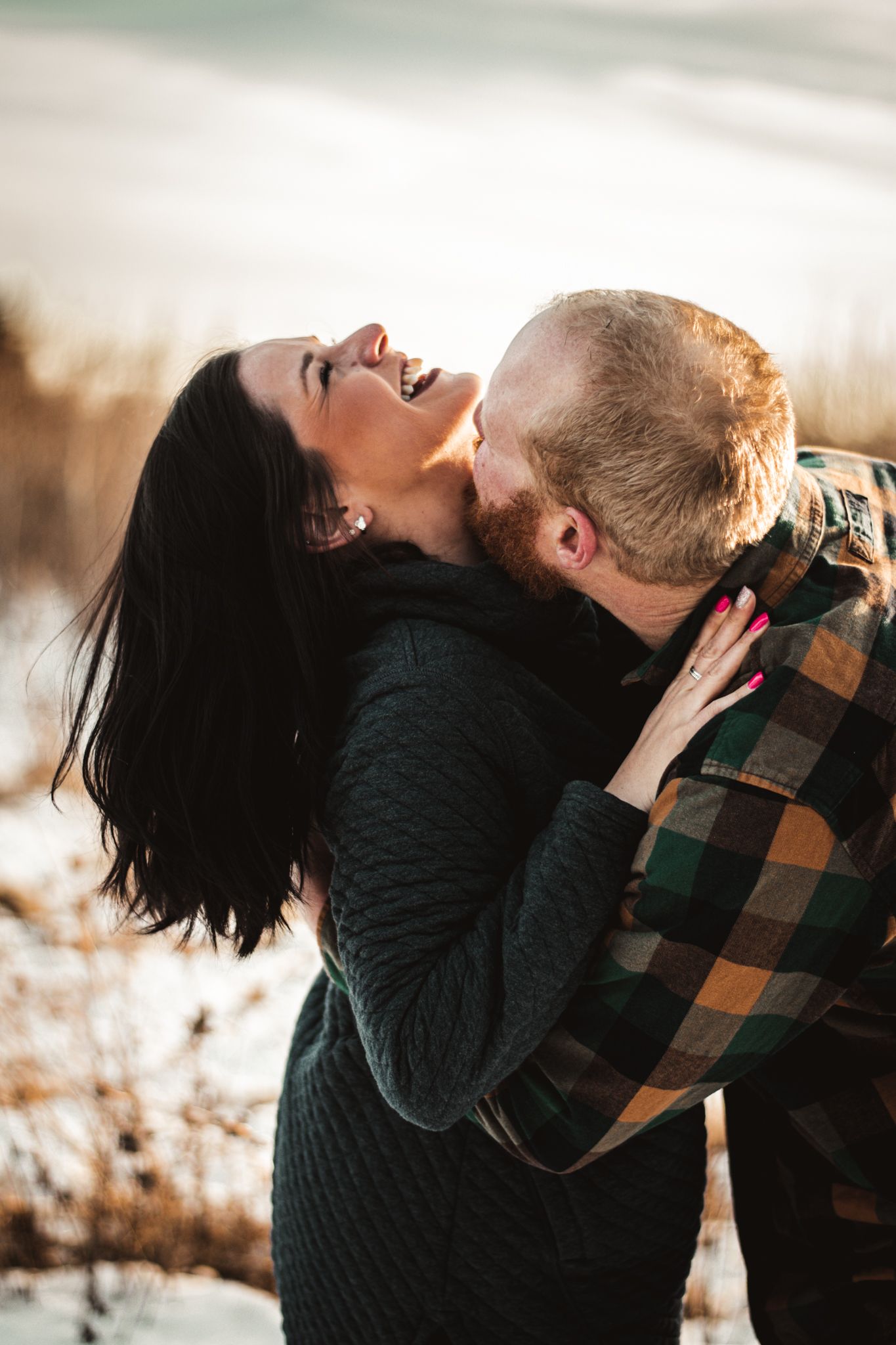 A joyful couple embracing and laughing together during sunset in casual winter attire.