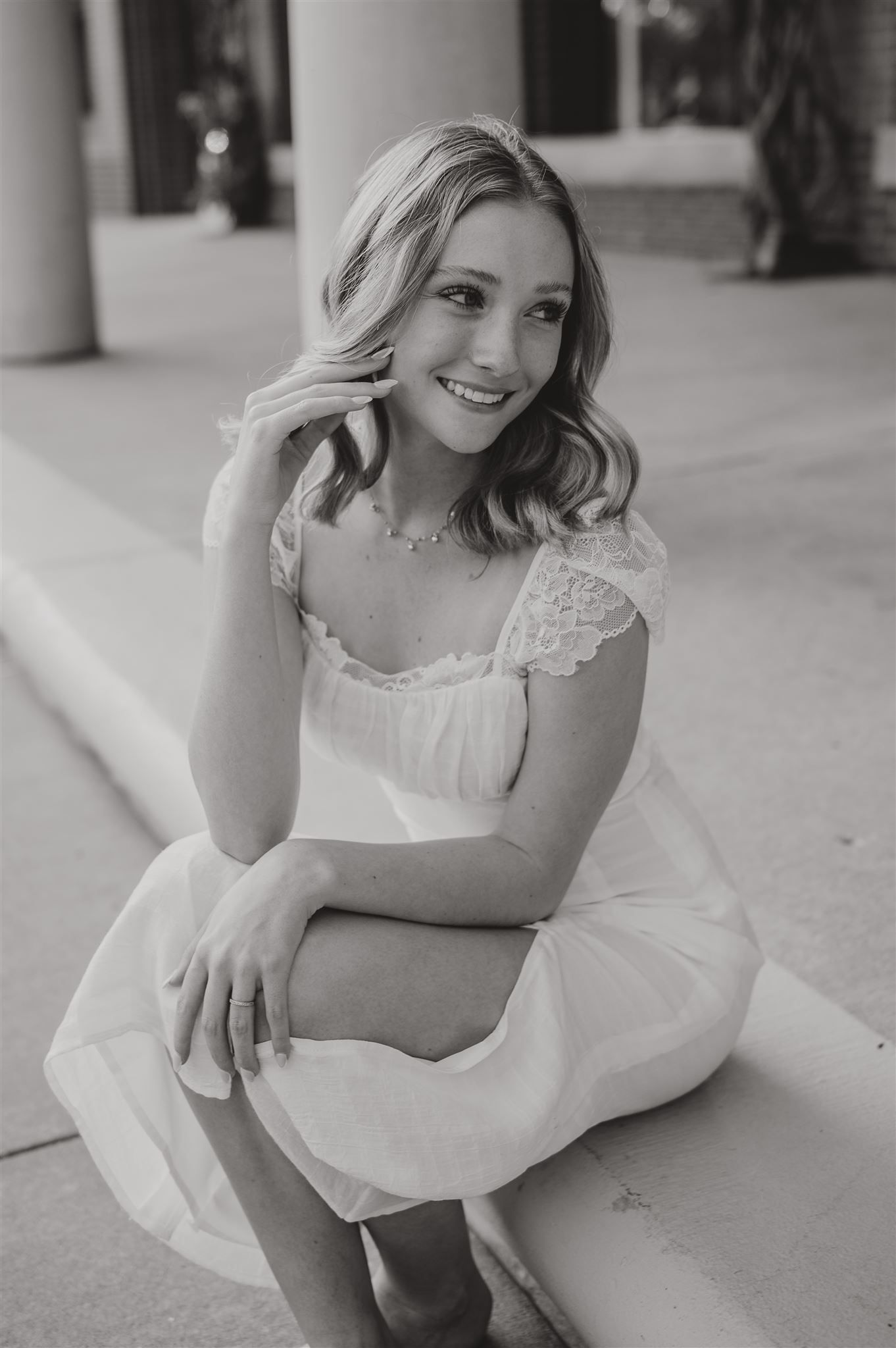 A black and white portrait of someone wearing a white lace dress sitting on concrete steps.