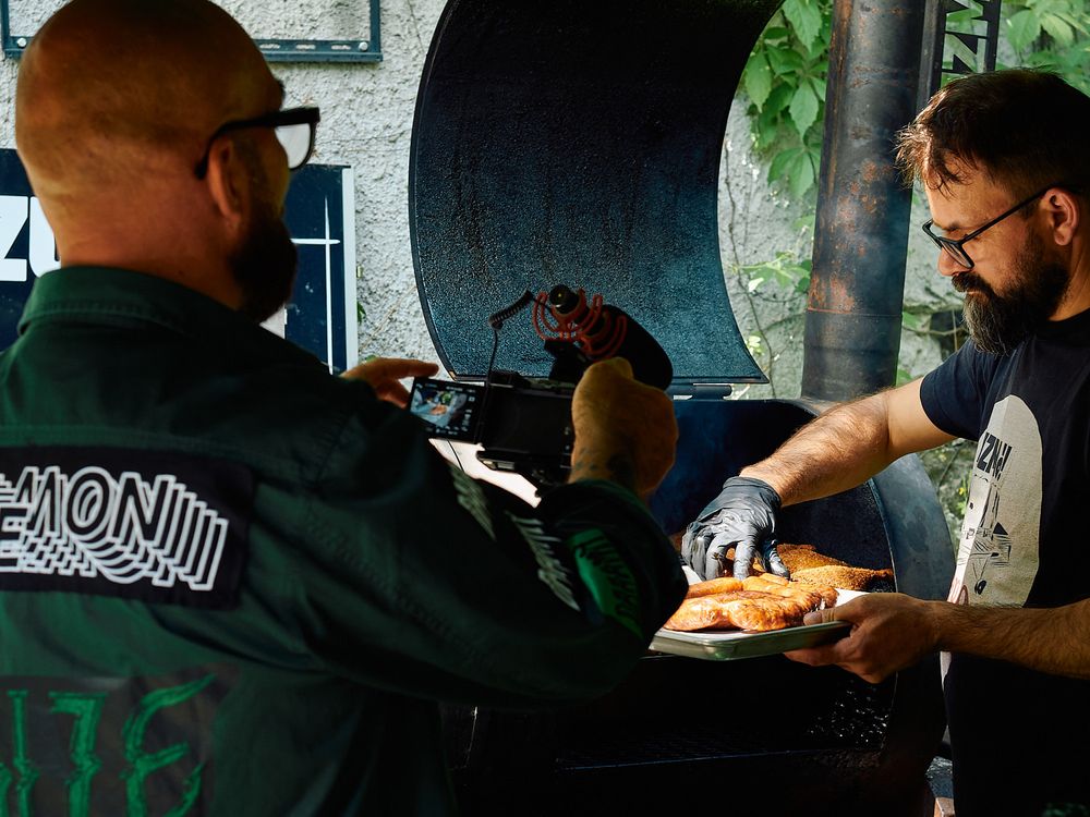 Two people preparing and plating food at an outdoor BBQ station.