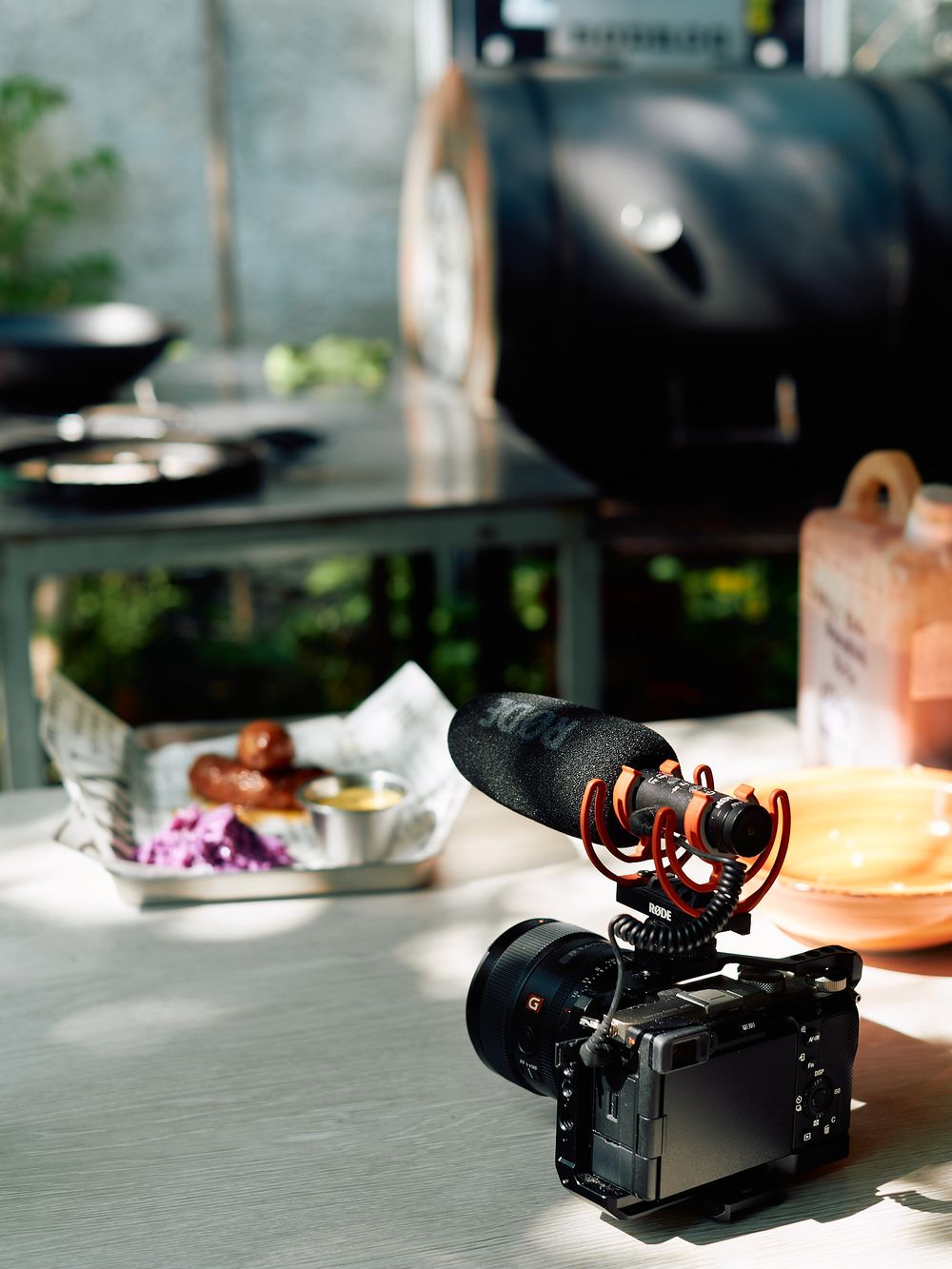 A digital camera with microphone setup on a table with food and plates in the background.