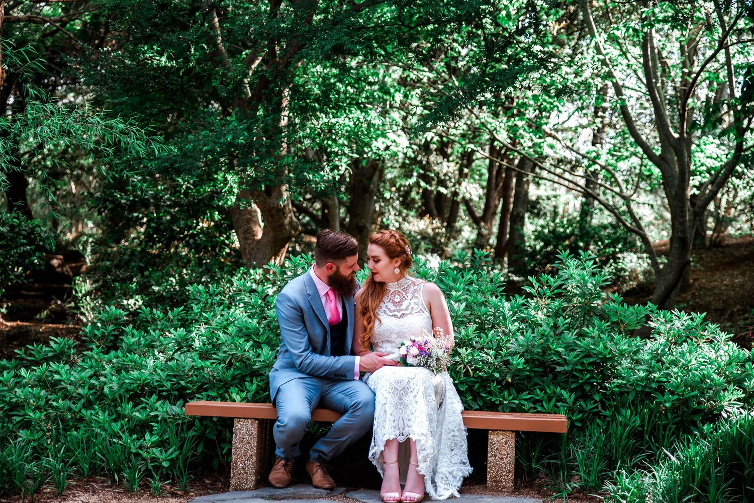 Couple sharing intimate moment on wooden bench in garden setting.