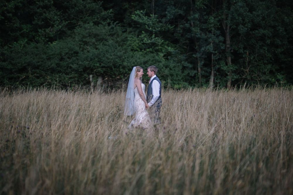 Romantic couple standing together in tall grass field at dusk.
