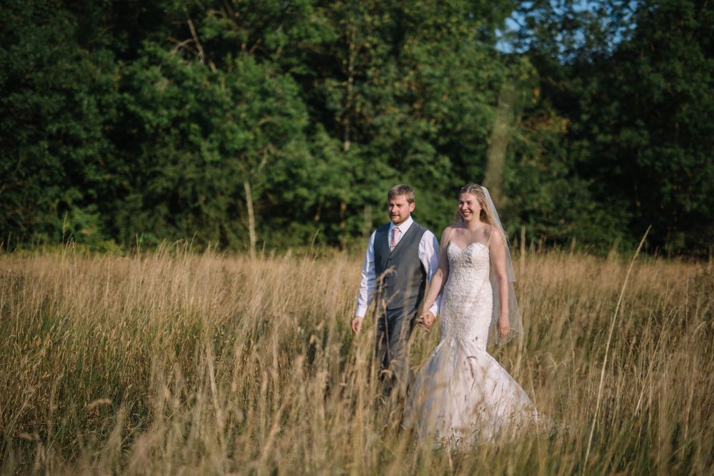 A couple stands together in a golden wheat field during their wedding day.