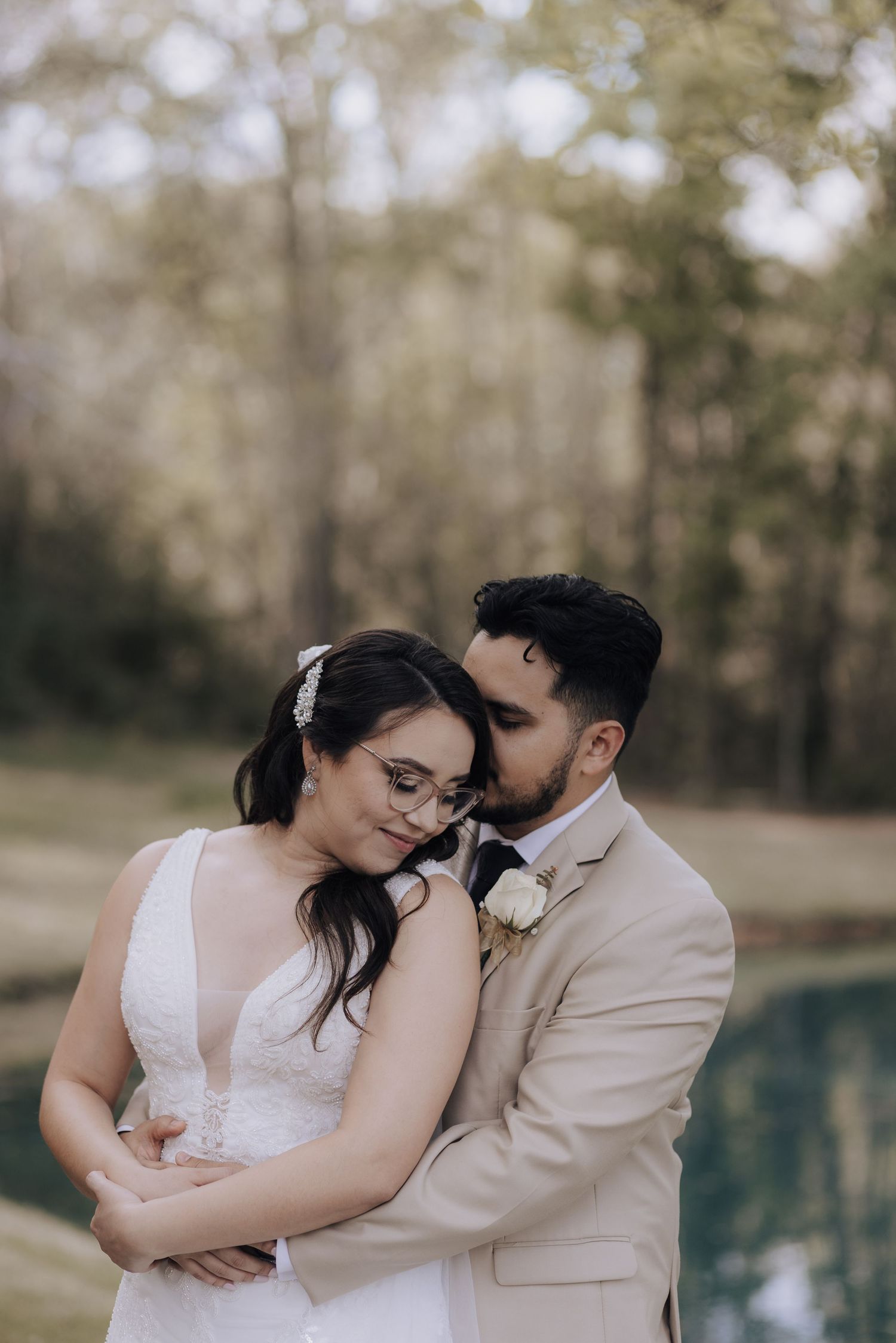 Tender moment between newlyweds in beige and white attire beside pool.