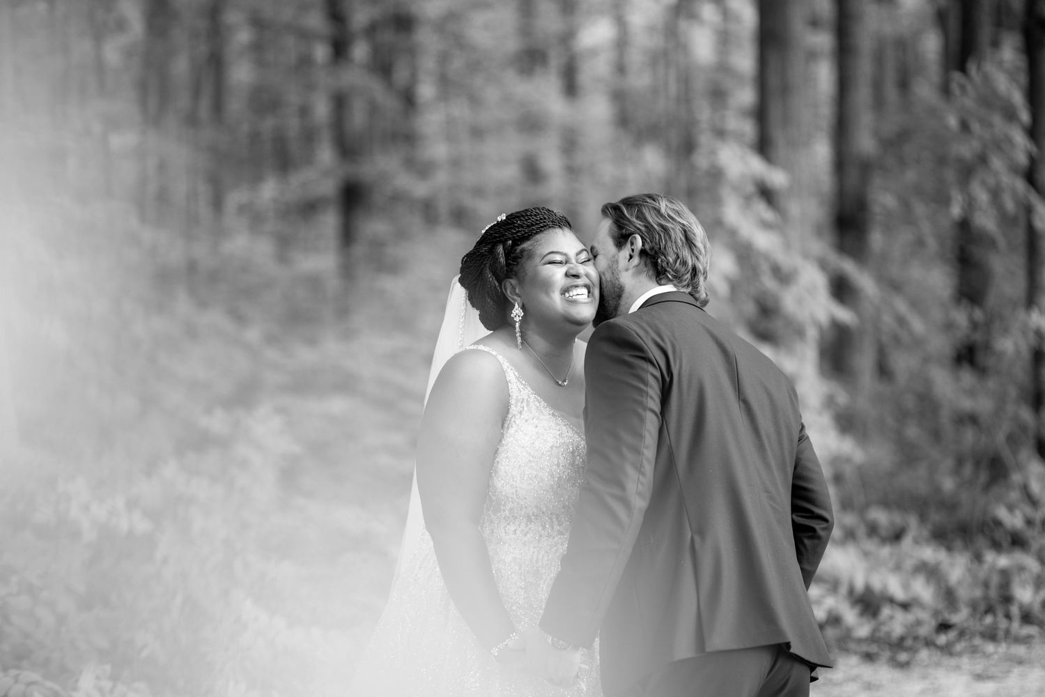 Black and white forest wedding portrait capturing tender moment between bride and groom.