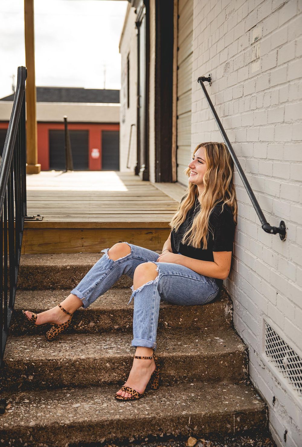 senior girl sitting on steps and leaning again a wall, laughing