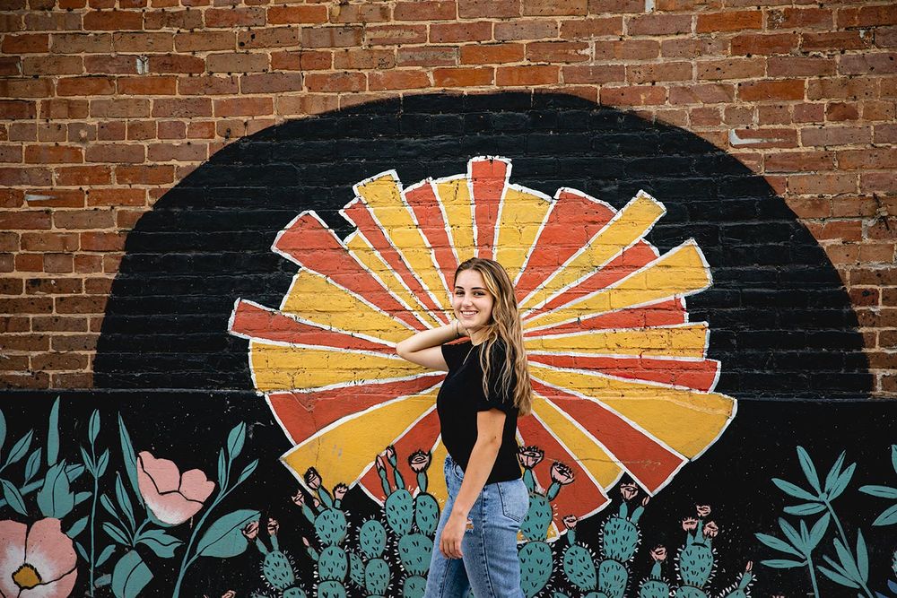 senior girl standing in front of mural on brick wall