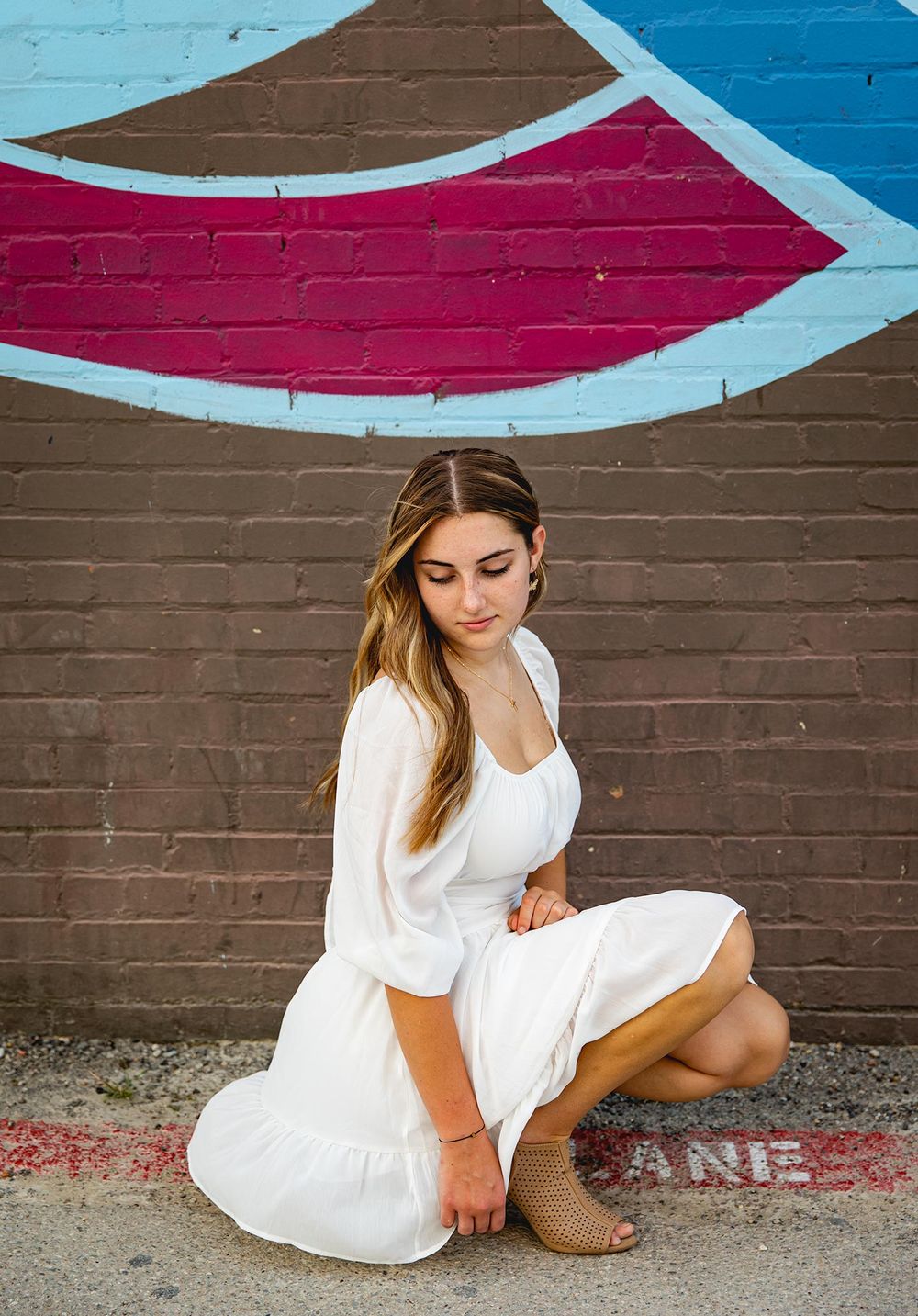 senior girl bent down in a white dress