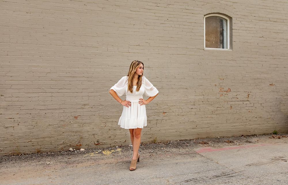 senior girl in white dress in front of painted brick