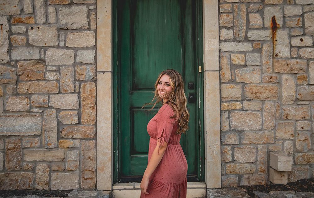senior photography session with girl looking back while standing in front of green door