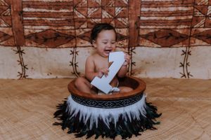 A baby plays with paper while sitting in a round basket adorned with feathers and tribal patterns.