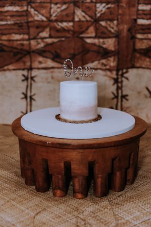 A simple white cake displayed on a rustic wooden cake stand with textured details.