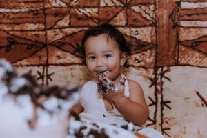 A happy child enjoys cake during a celebratory photoshoot against a brown background.