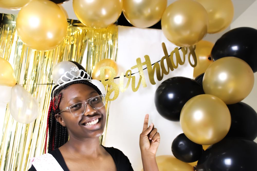A celebratory scene with gold and black balloons against a backdrop with metallic fringe.