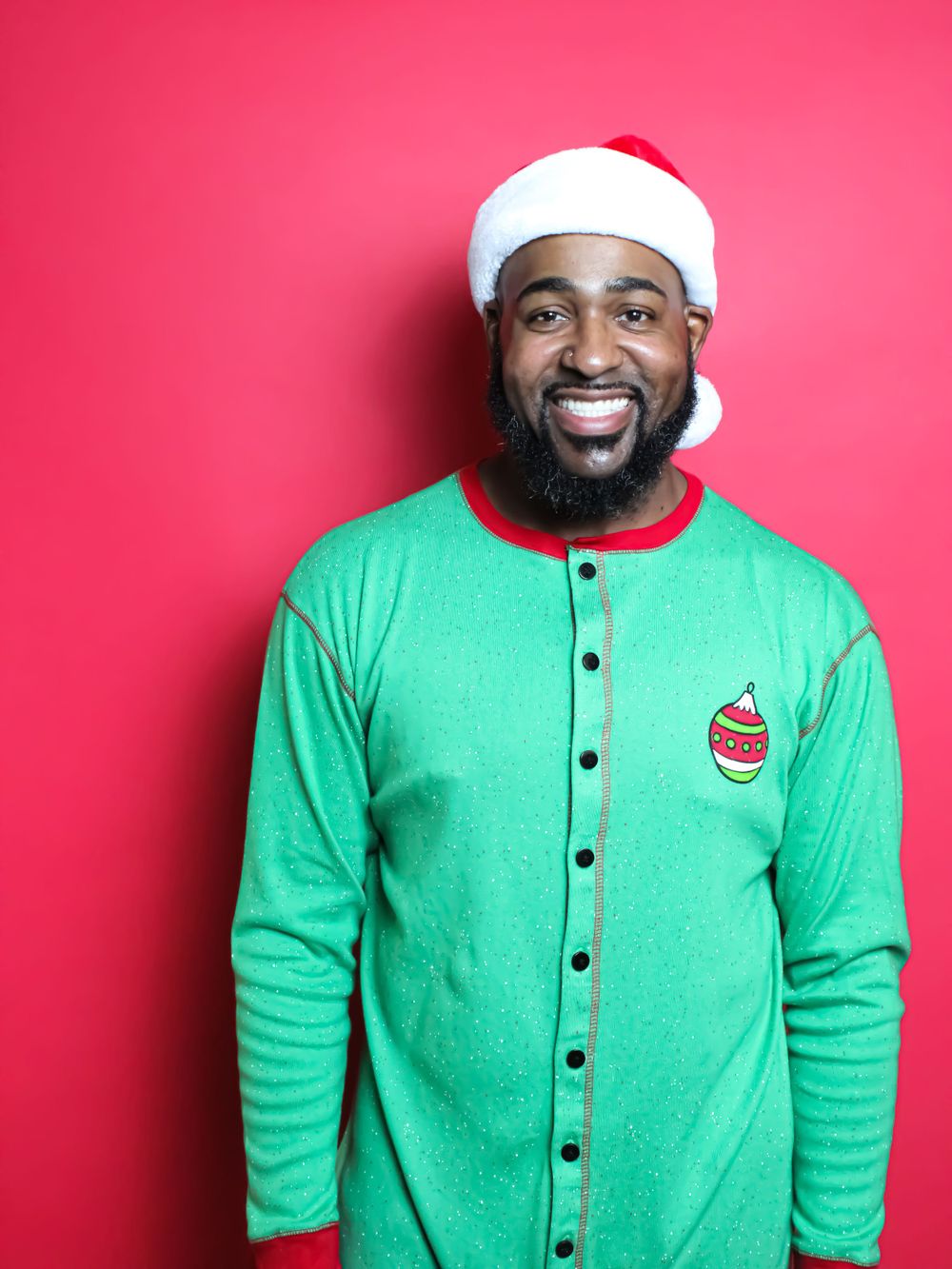 A joyful holiday portrait with Santa hat and green button-up sweater against red backdrop.