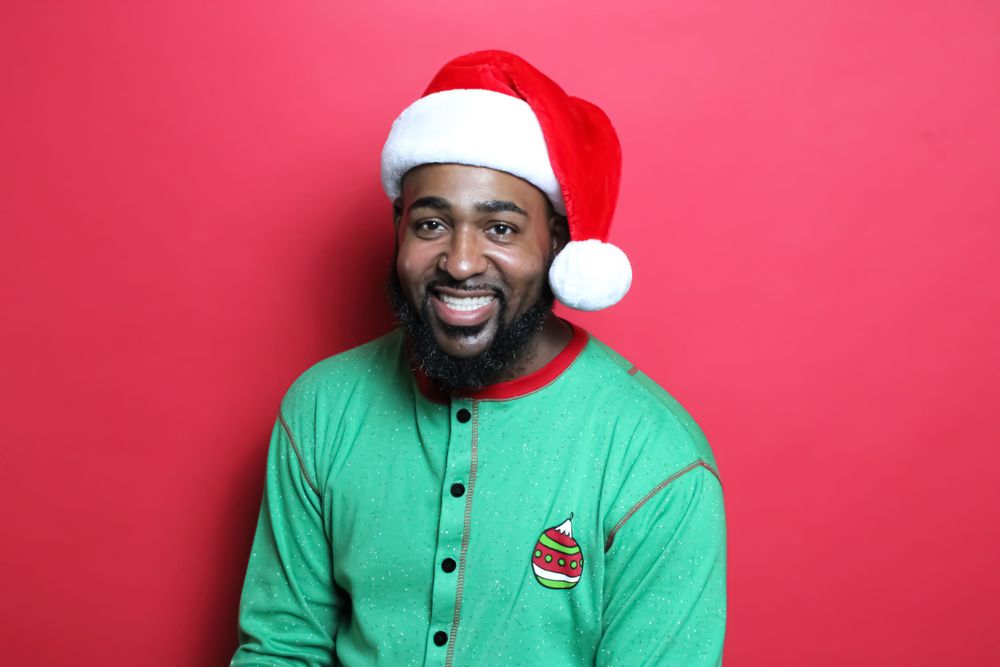 A festive holiday portrait in green attire and Santa hat against a red background.