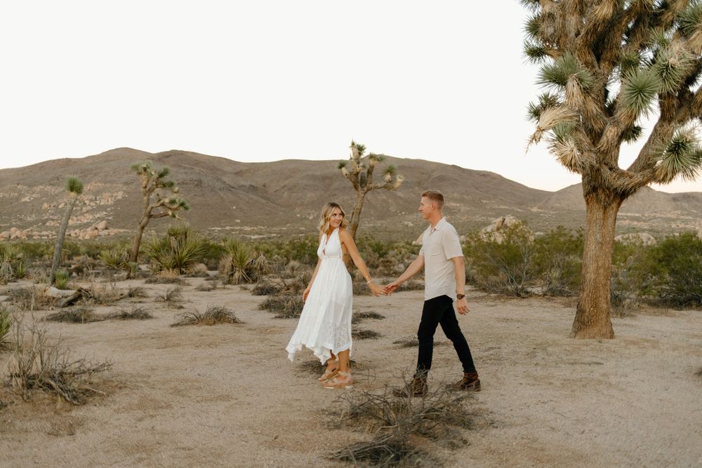 Romantic desert photoshoot with couple walking among Joshua trees and desert plants.