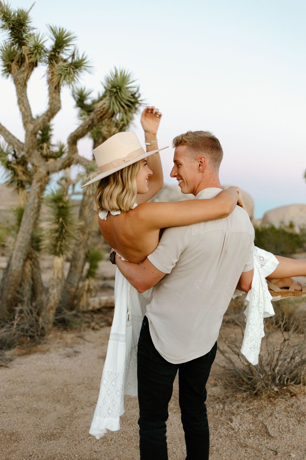 Playful couple embracing in desert setting with Joshua trees and mountains.