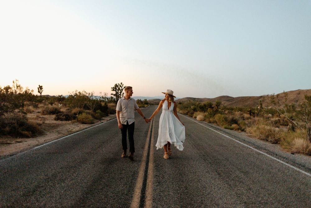 Couple walking together on empty desert road at sunset surrounded by Joshua trees.