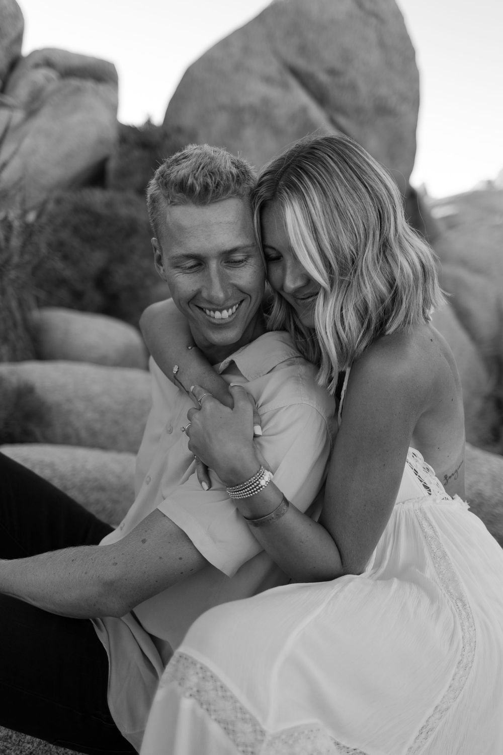 Black and white portrait of couple sharing intimate moment against desert rock formations.