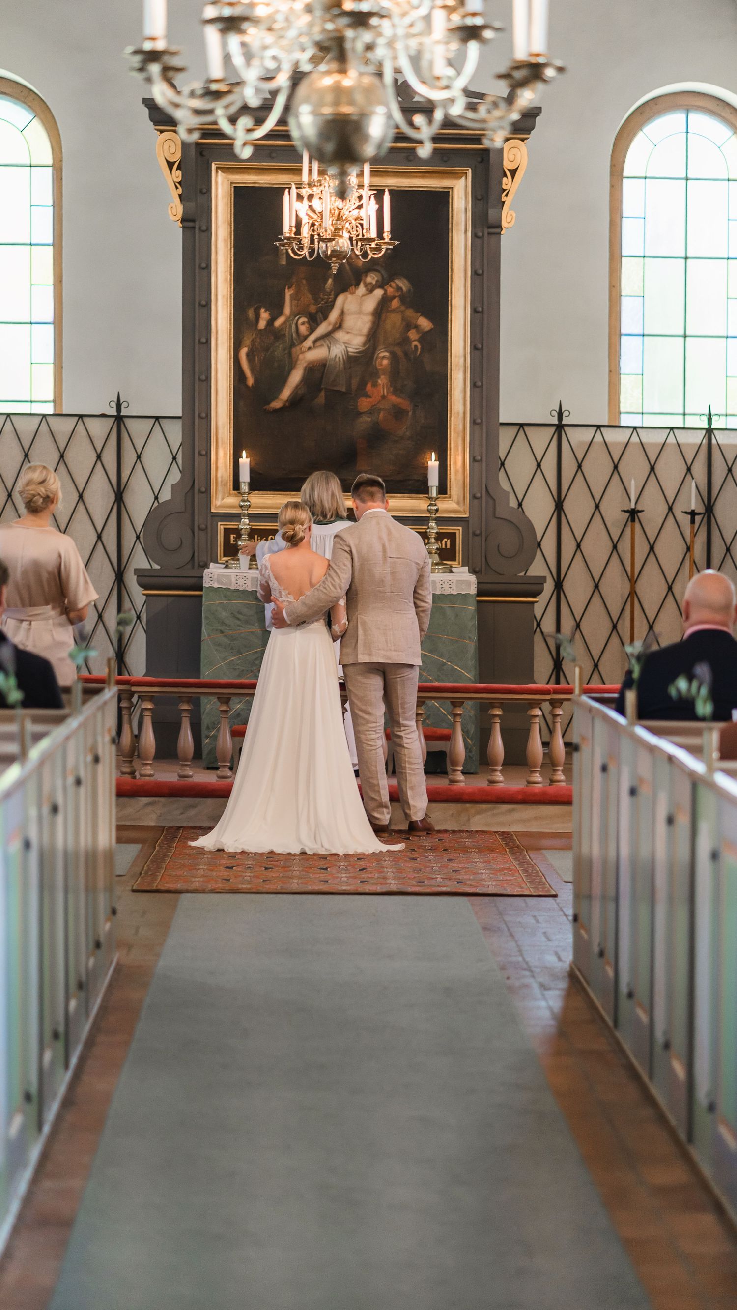 Bride and groom stand together at church altar before a large religious painting during wedding ceremony.