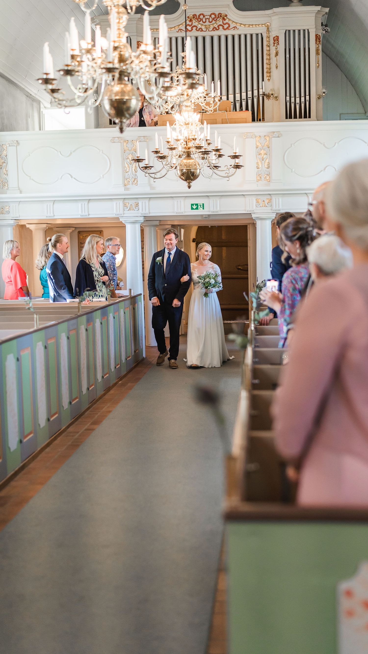 Bride in white gown walks down church aisle escorted by a man in a suit during wedding ceremony.