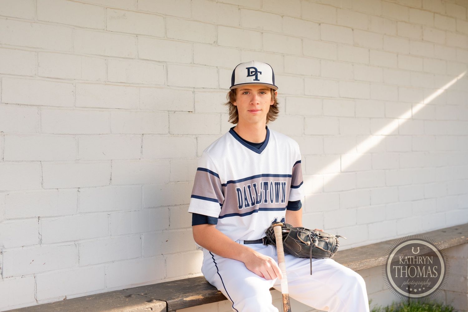 Baseball player in Darlington uniform sits in sunlit dugout with glove.