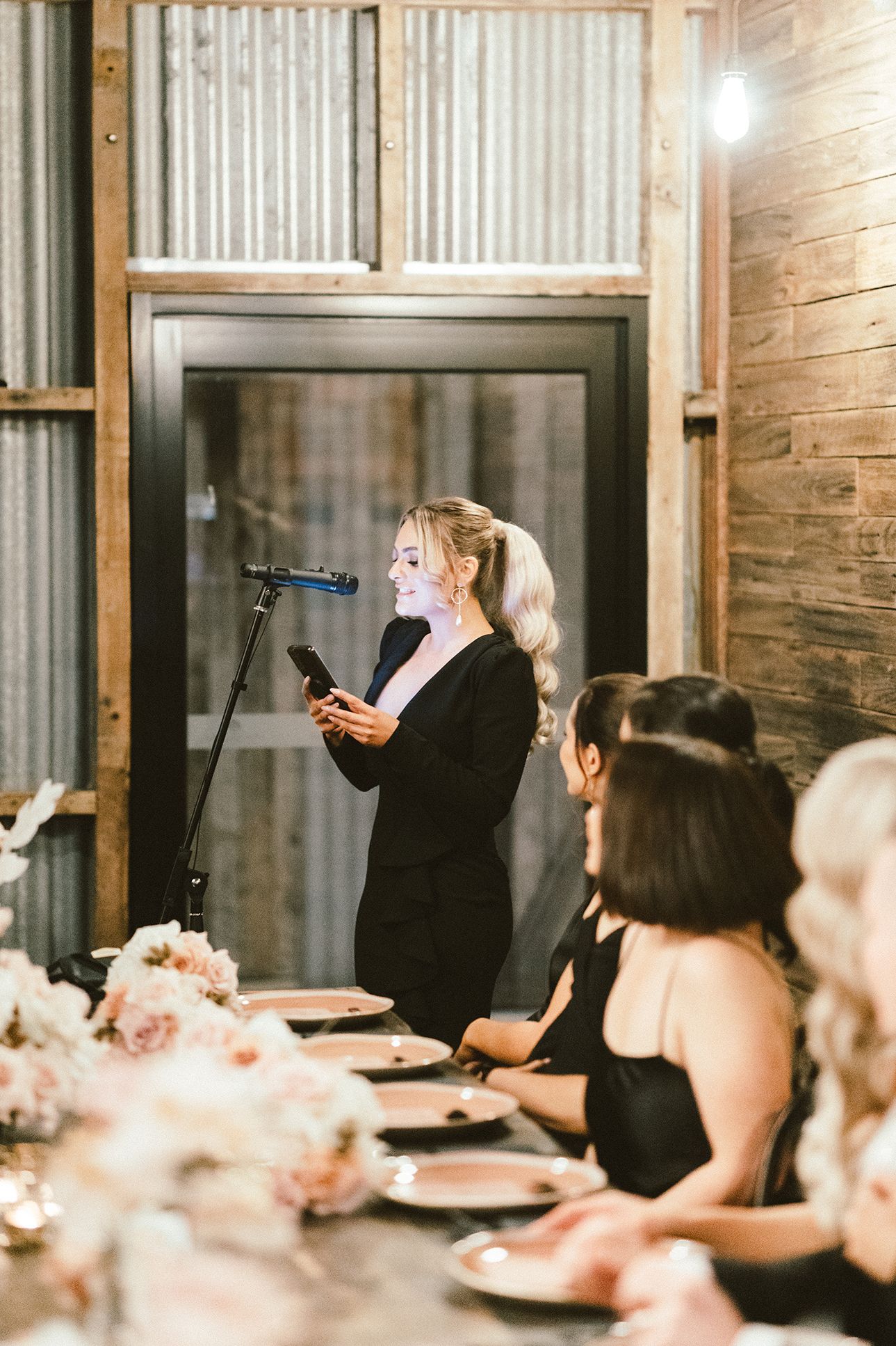 Wedding toast being given at reception with rustic wood walls and floral decorations.