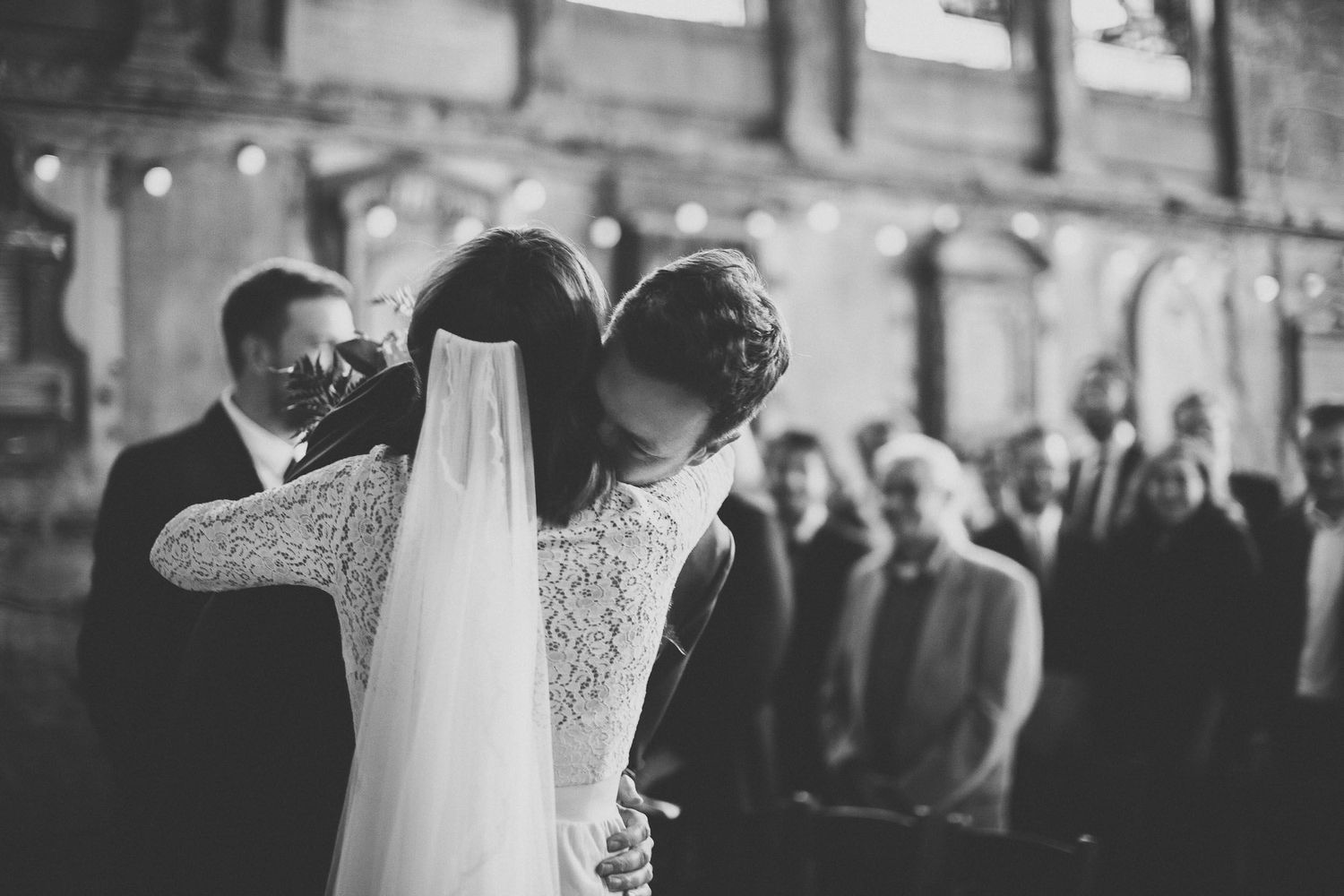 Bride and groom embrace at the church with guests in background