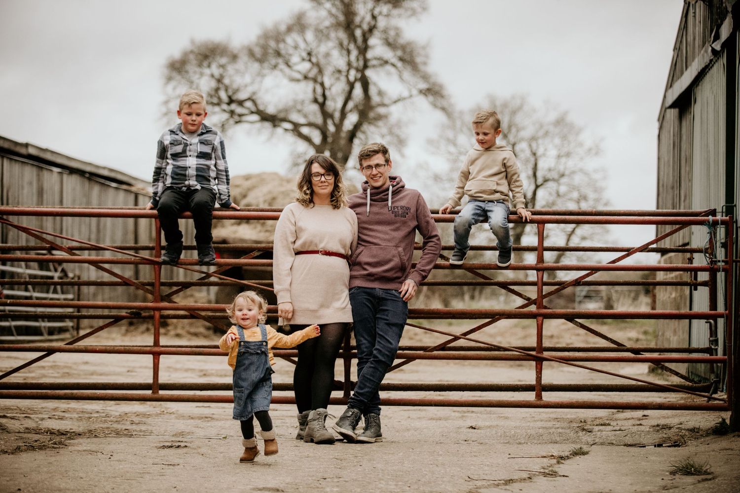 A family poses casually on a rustic metal gate in a rural farm setting.