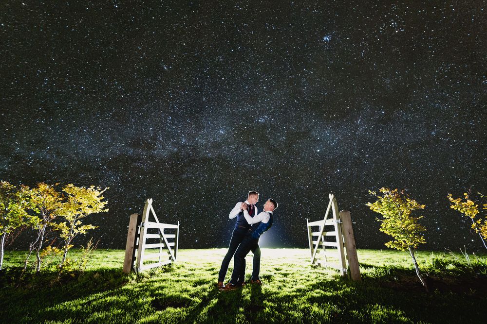 Wedding couple poses under starry night sky with illuminated trees.
