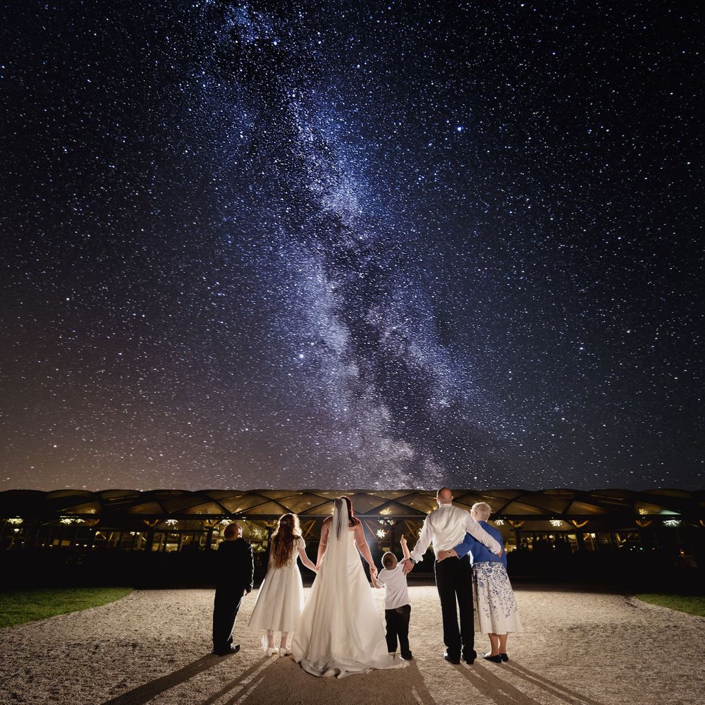 Wedding party silhouetted against stunning Milky Way galaxy in night sky.