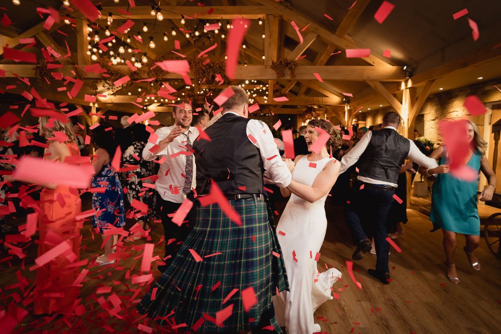 Wedding celebration with red confetti flying through air in warm-lit reception venue.