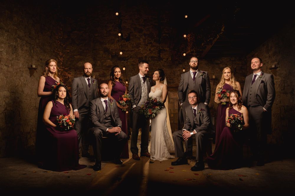 Wedding party poses in dramatic lighting against stone wall backdrop.