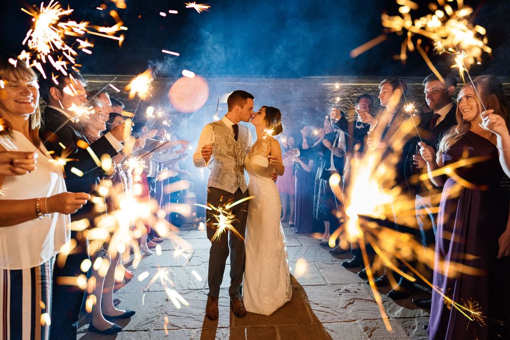 Wedding celebration with sparklers creating trails of light against blue evening sky.
