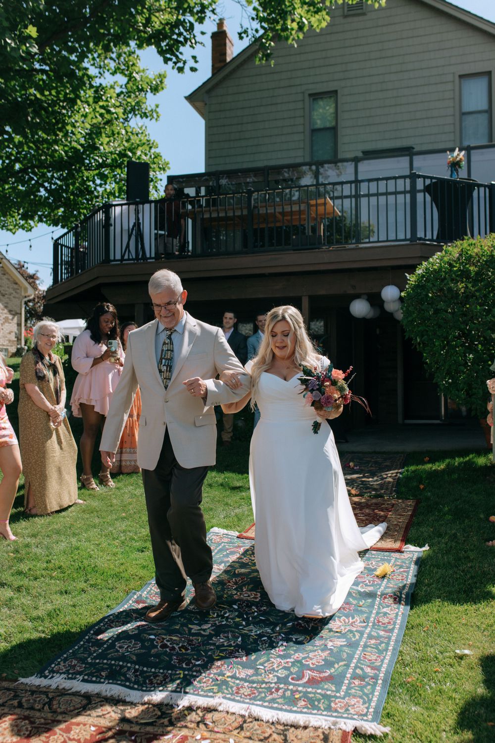 A wedding ceremony processional on a decorated outdoor path with guests watching.